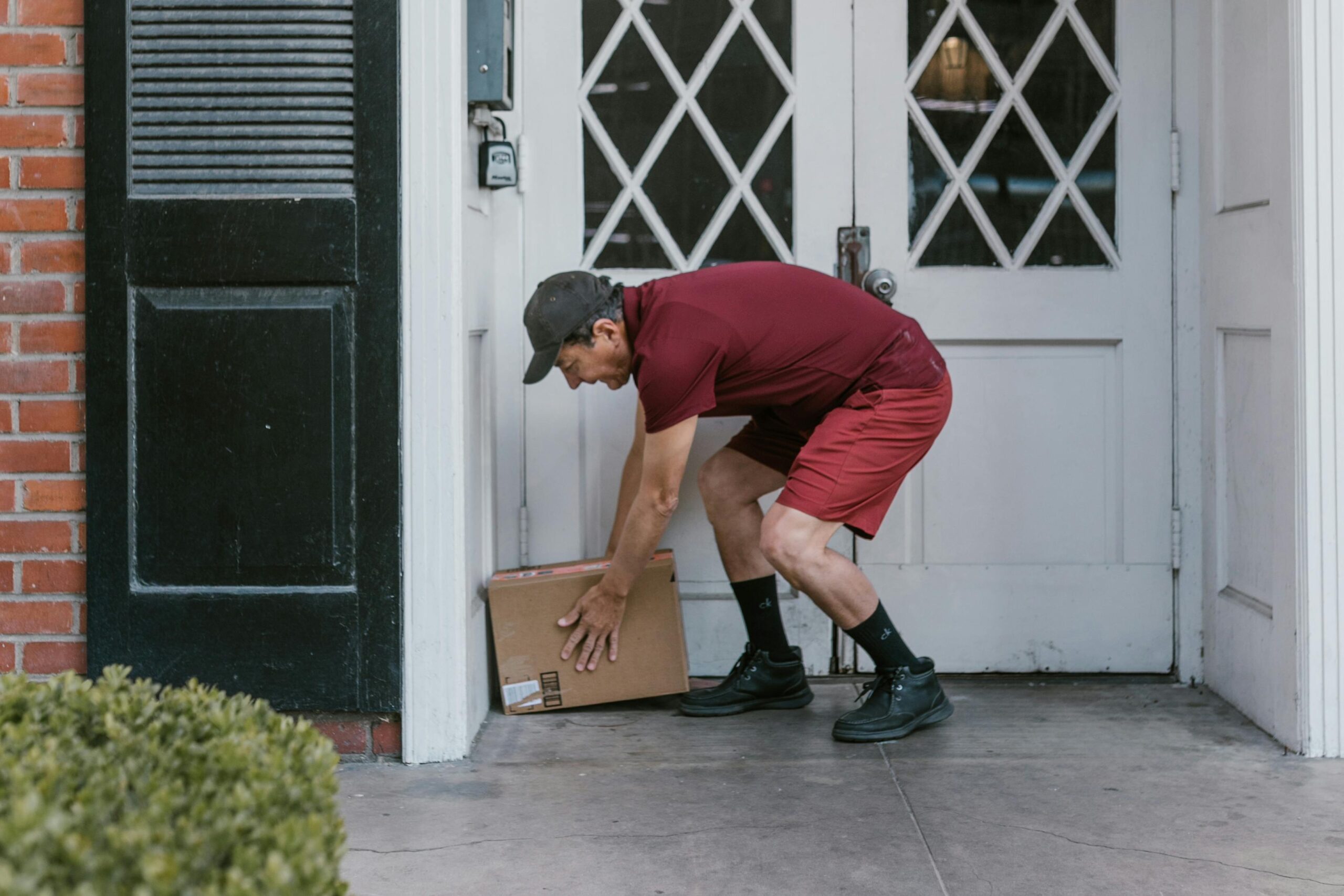 Home Delivery person in red uniform leaving a package at a home's front door.